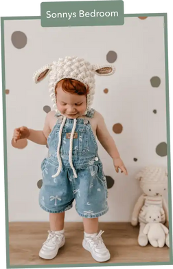 Adorable toddler wearing denim overalls, white sneakers, and a knitted bunny hat.